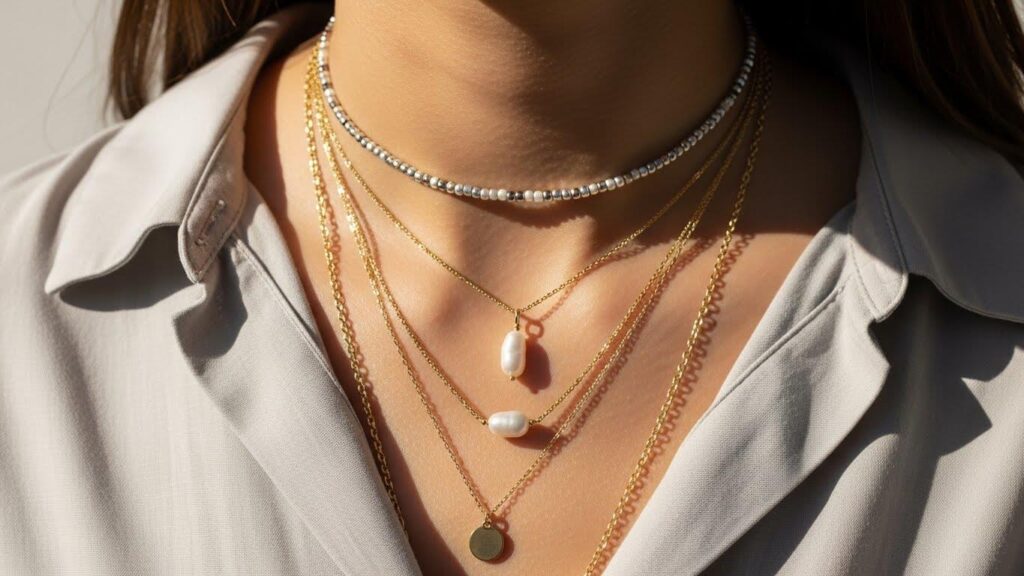 Dekolt kobiety w koszuli, z kilkoma warstwami delikatnych naszyjników o różnej długości.